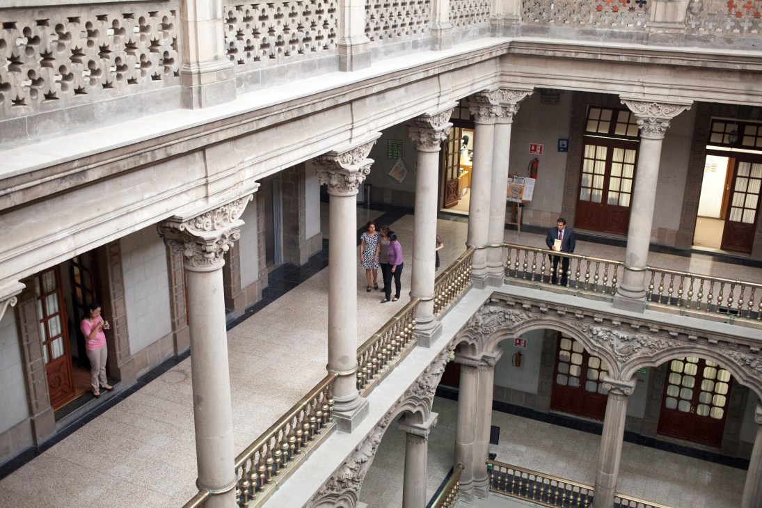 Interior courtyard of the National Palace with classical columns, ornate railings, and several visitors walking through the architectural space.