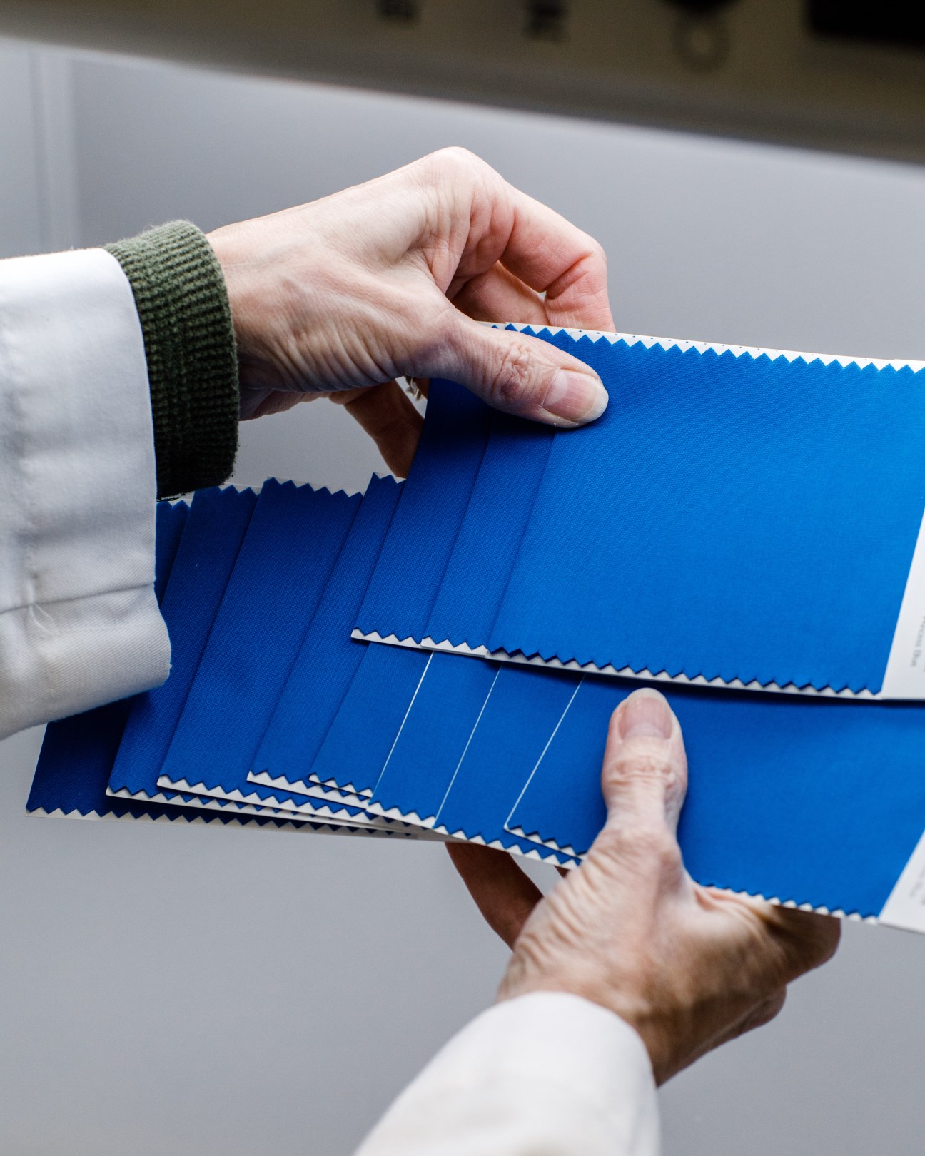 Two hands holding blue fabric swatches with scalloped edges from Pantone's color collection.
