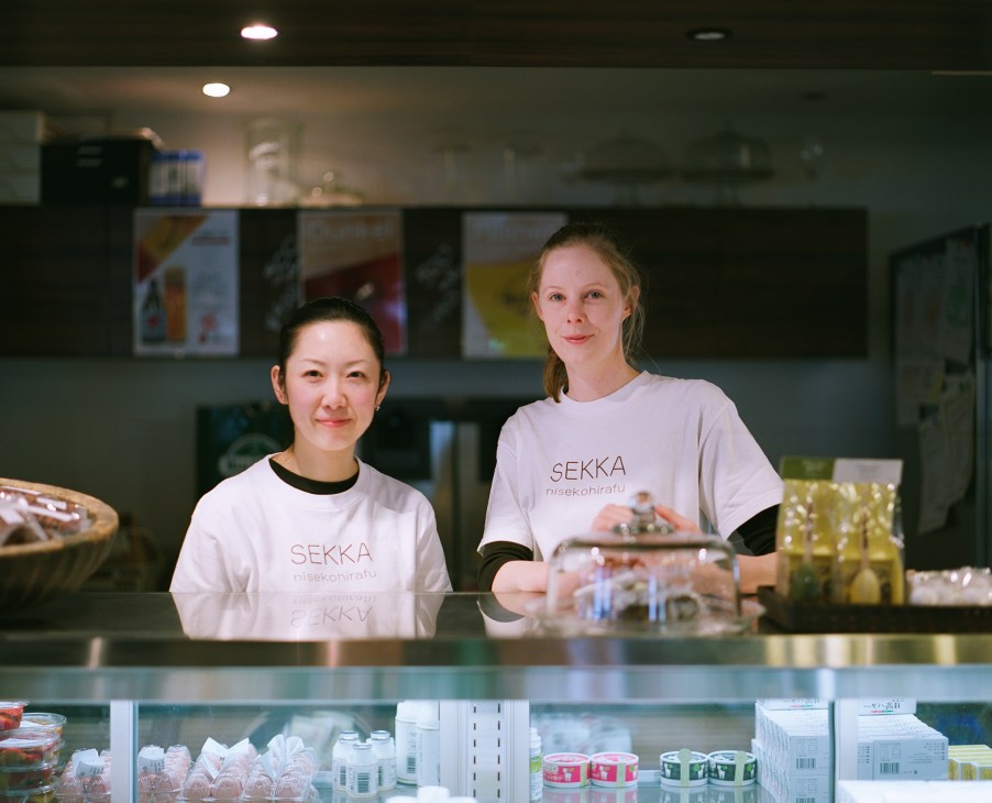 Two staff members stand behind a counter at J-Sekka deli wearing branded t-shirts.