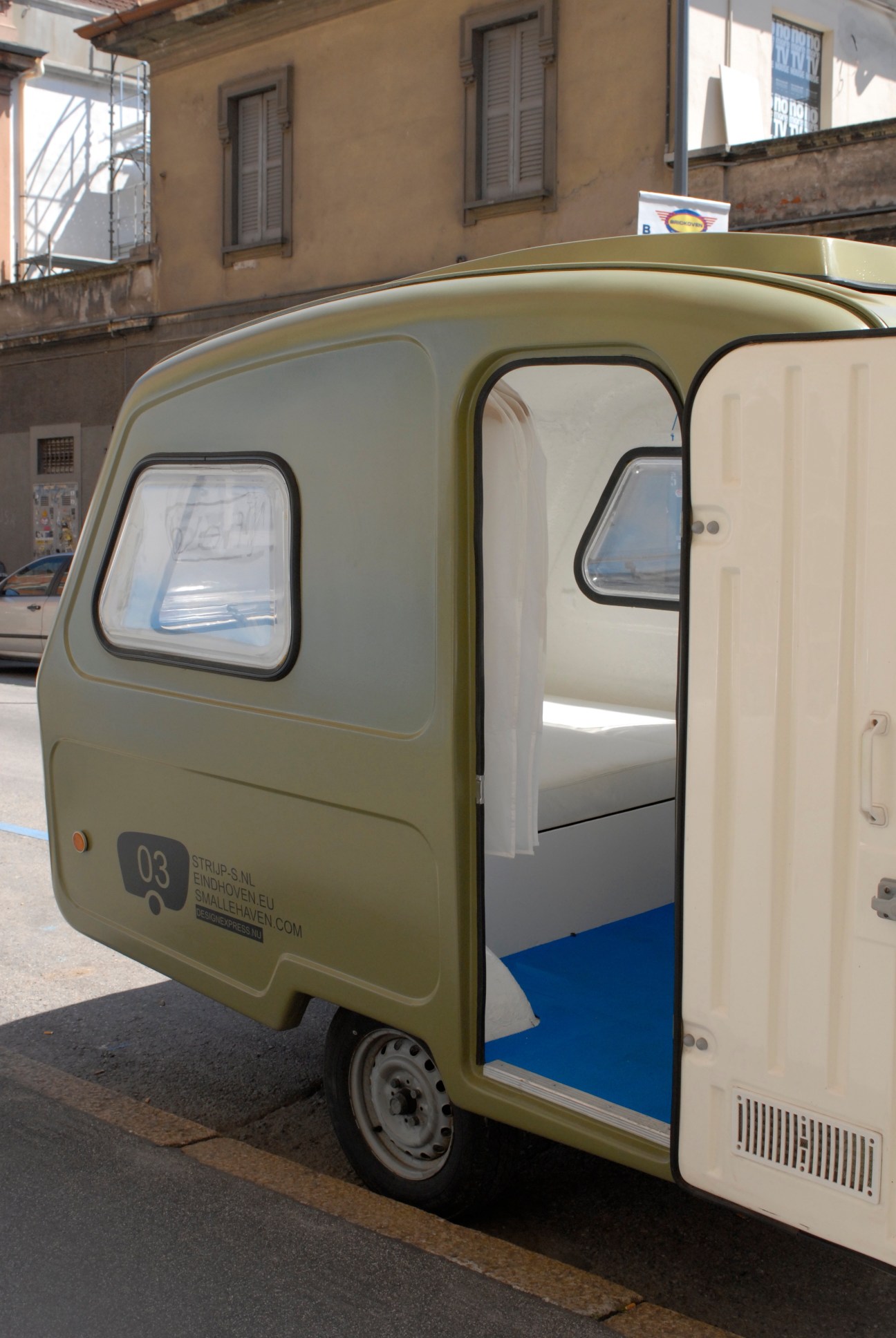 Olive-green and cream Smalle Haven caravan with open door displayed on a city street.