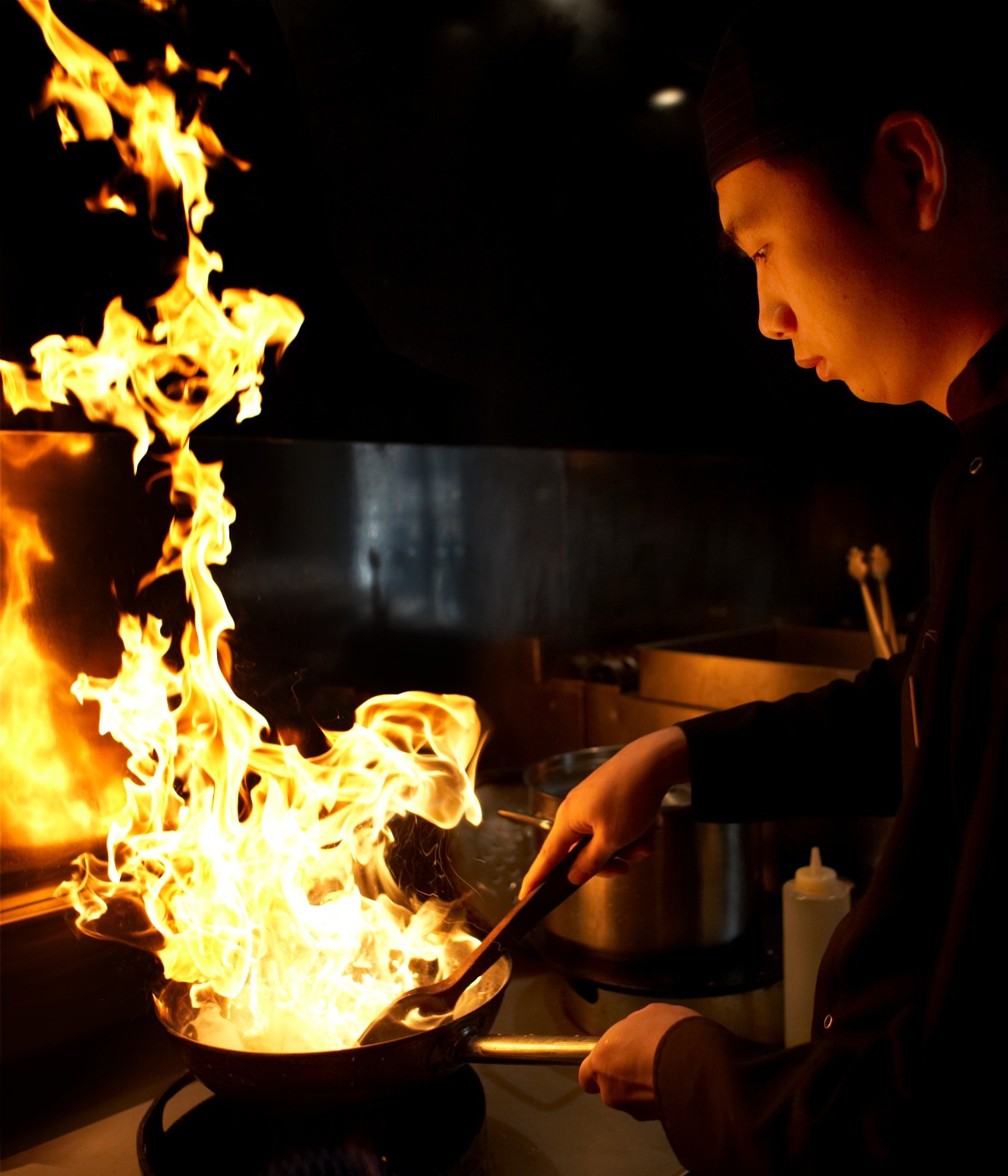 Chef at Nippon restaurant performing a flaming tableside cooking technique with fire in a pan.