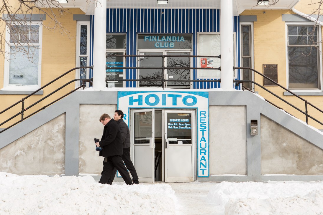 The Finlandia Club building exterior with Hoito restaurant entrance below, snow on ground, two people walking past.
