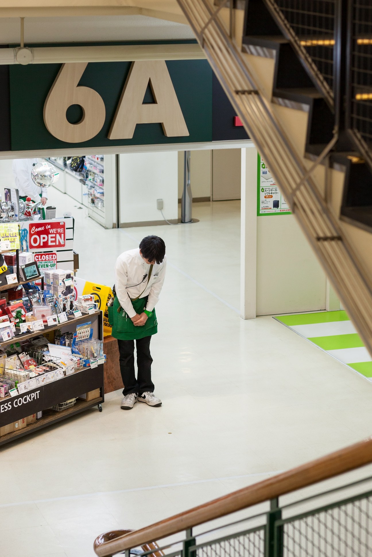Tokyu Hands staff member in green apron bowing at floor 6A entrance during store opening.