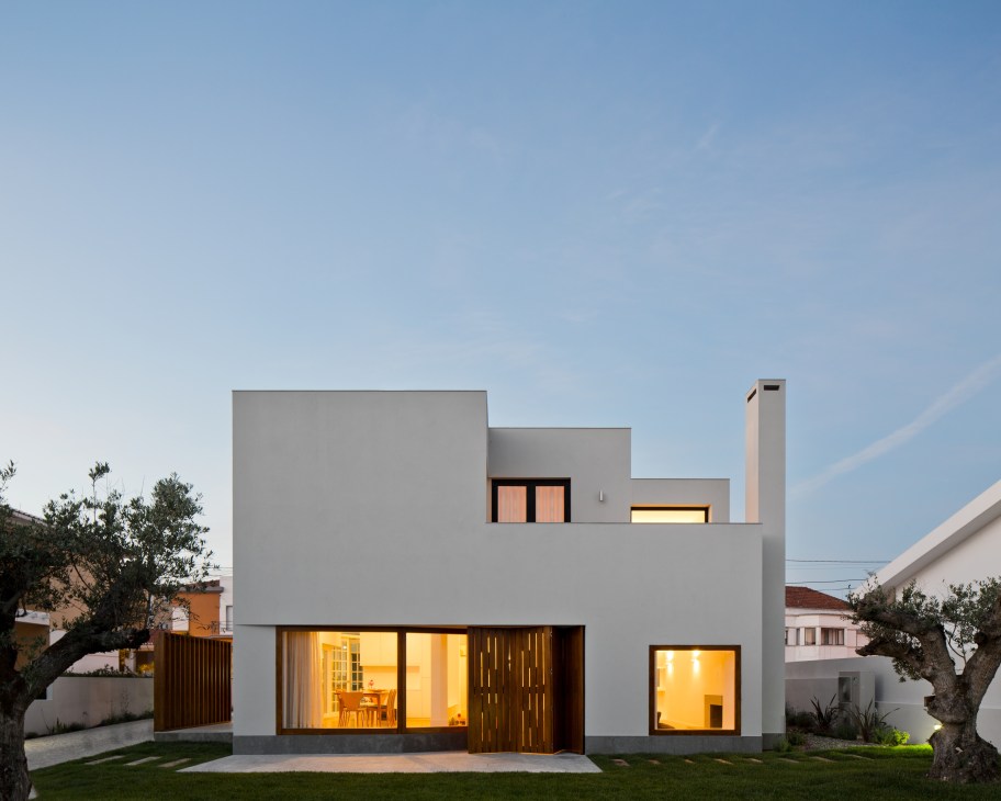 Modern white house with wooden doors and warm-lit windows at dusk in Sintra, Portugal.