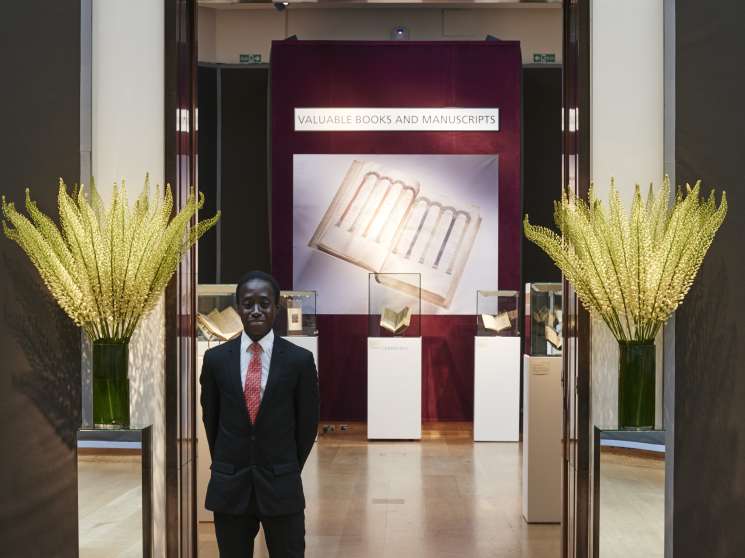 Man in dark suit standing in Christie's auction gallery with valuable books display.
