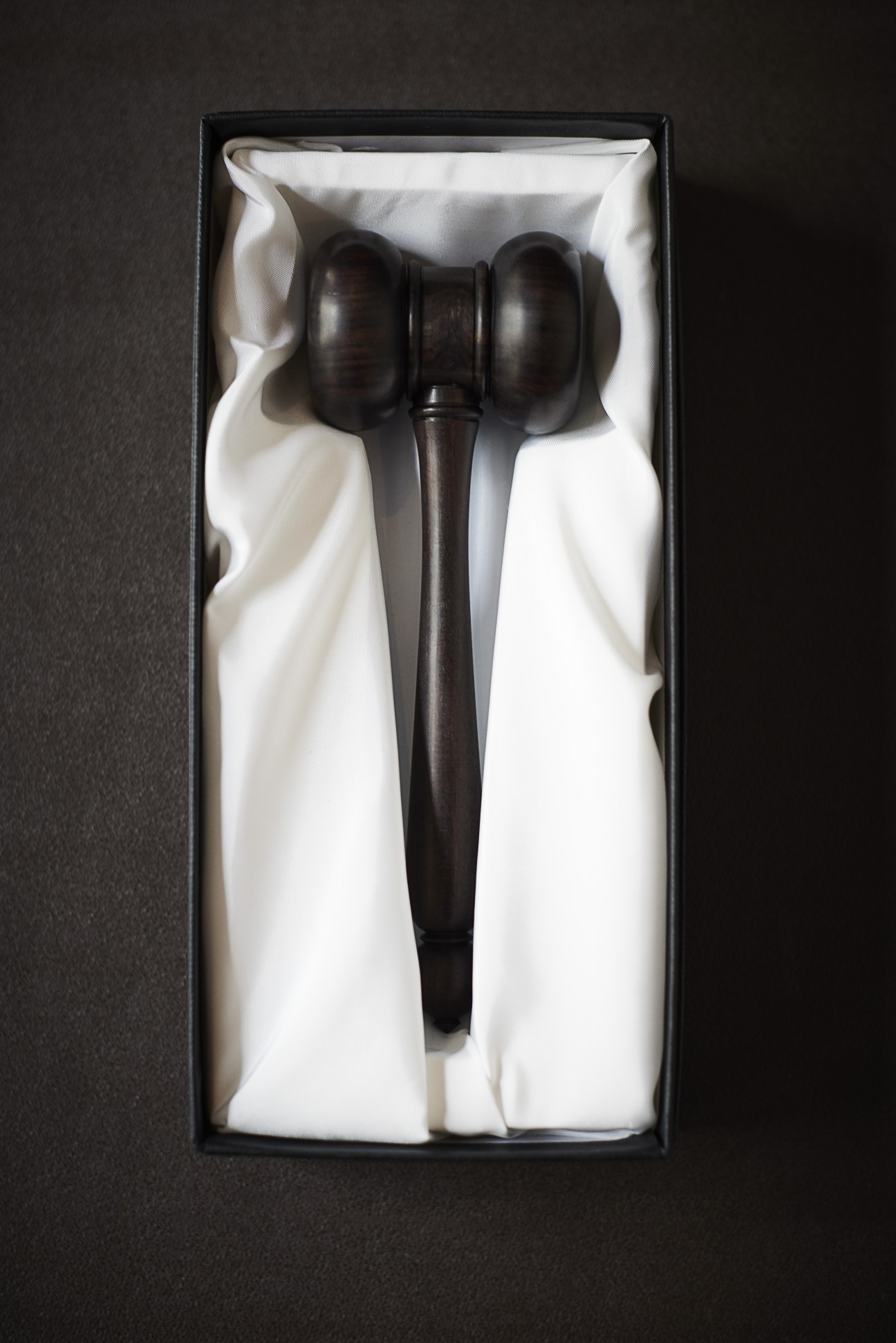 Dark wooden gavel with rounded head nestled in white tissue paper inside a black presentation box.
