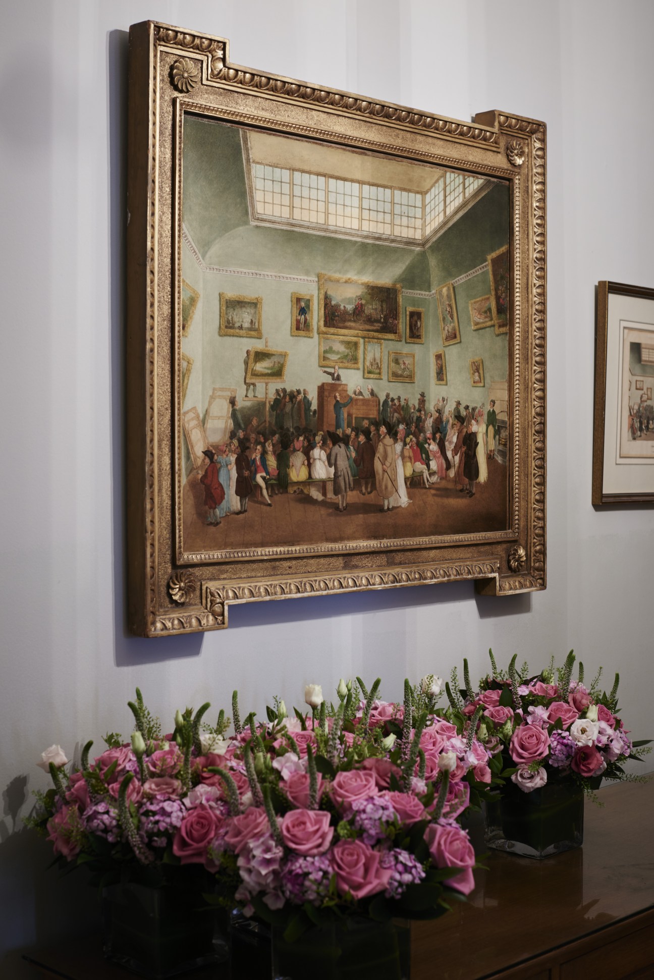 Ornate gold-framed painting depicting a historic auction scene hung above pink flowers in Christie's boardroom.
