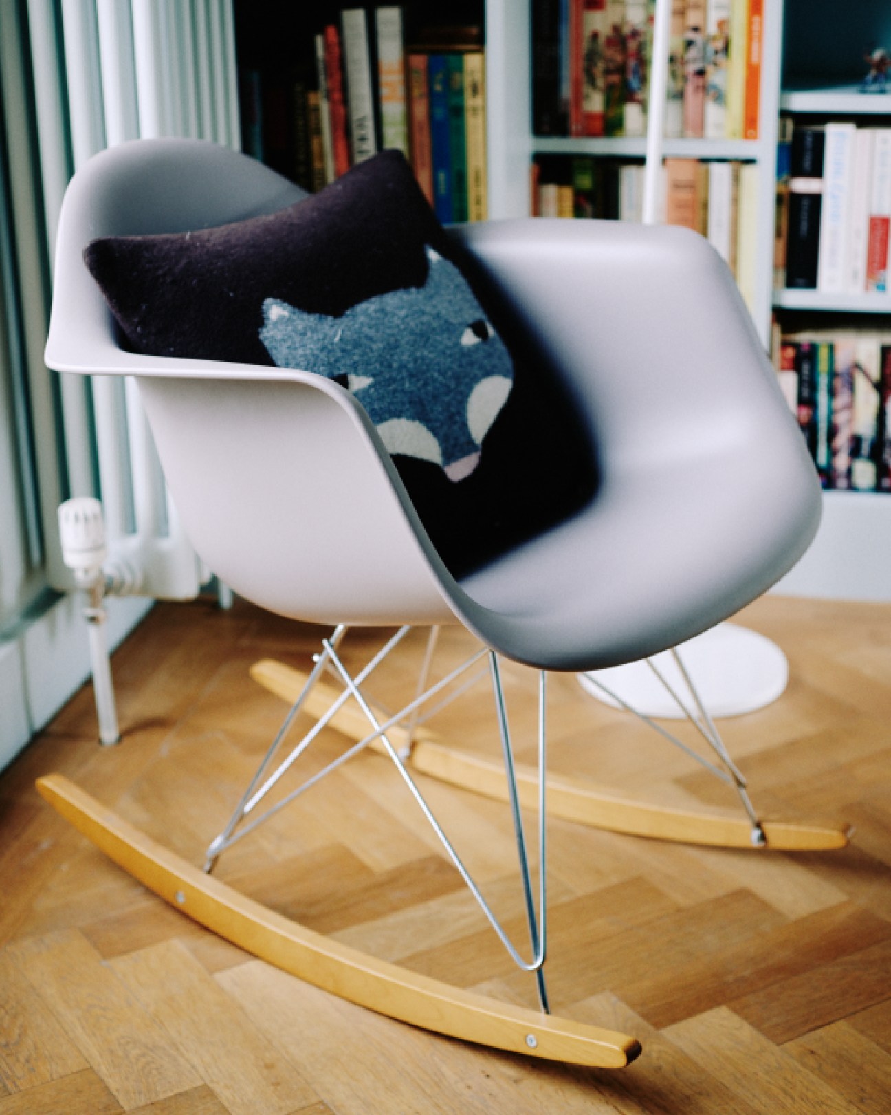 White molded chair with wooden rockers topped with black and blue patterned cushions in a home library setting.