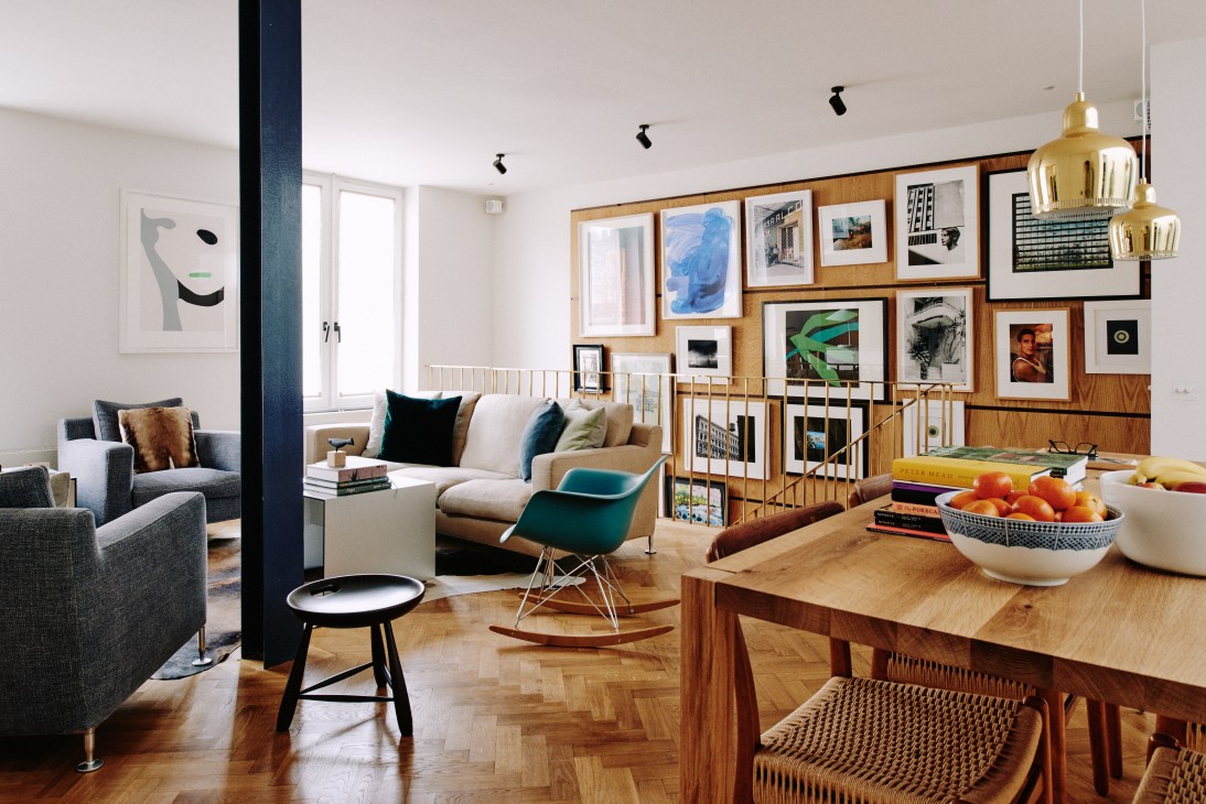 Modern living room with oak gallery wall, e15 table, and brass Alvar Aalto pendant lamps.