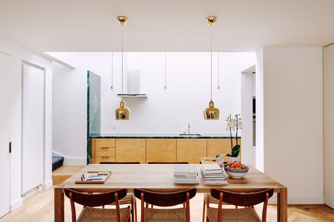 Kitchen with oak panel cupboards, green marble countertop, brass pendant lights and wooden dining table with chairs.