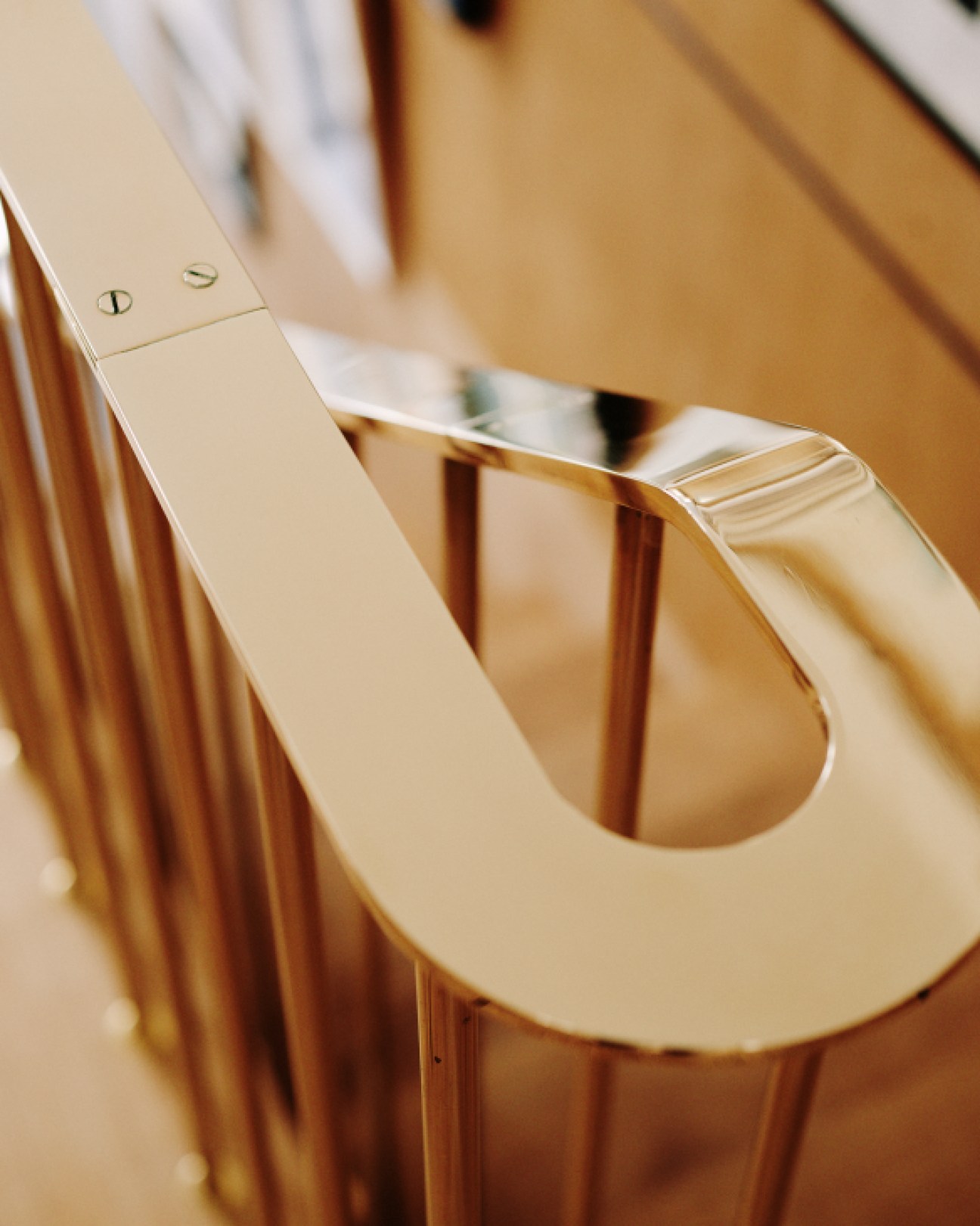 Custom brass handrail with horizontal ridging detail on a wooden stairwell.