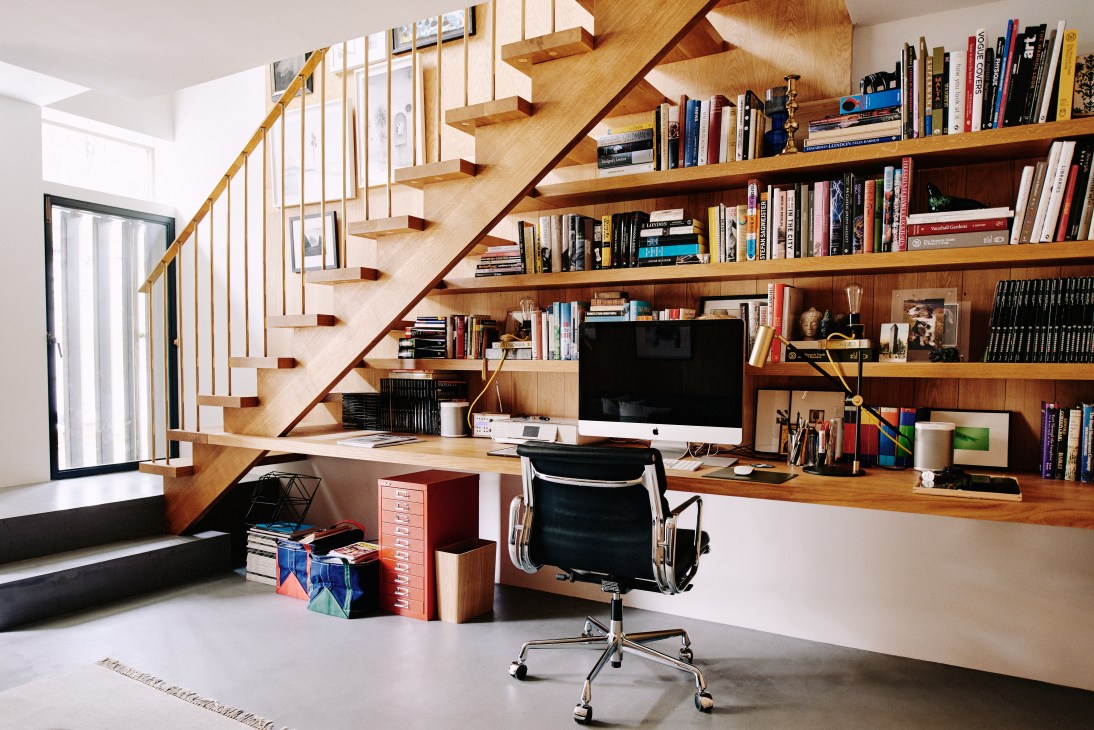 A wooden staircase with oak steps and custom brass handrail, with built-in shelving filled with books along the wall.