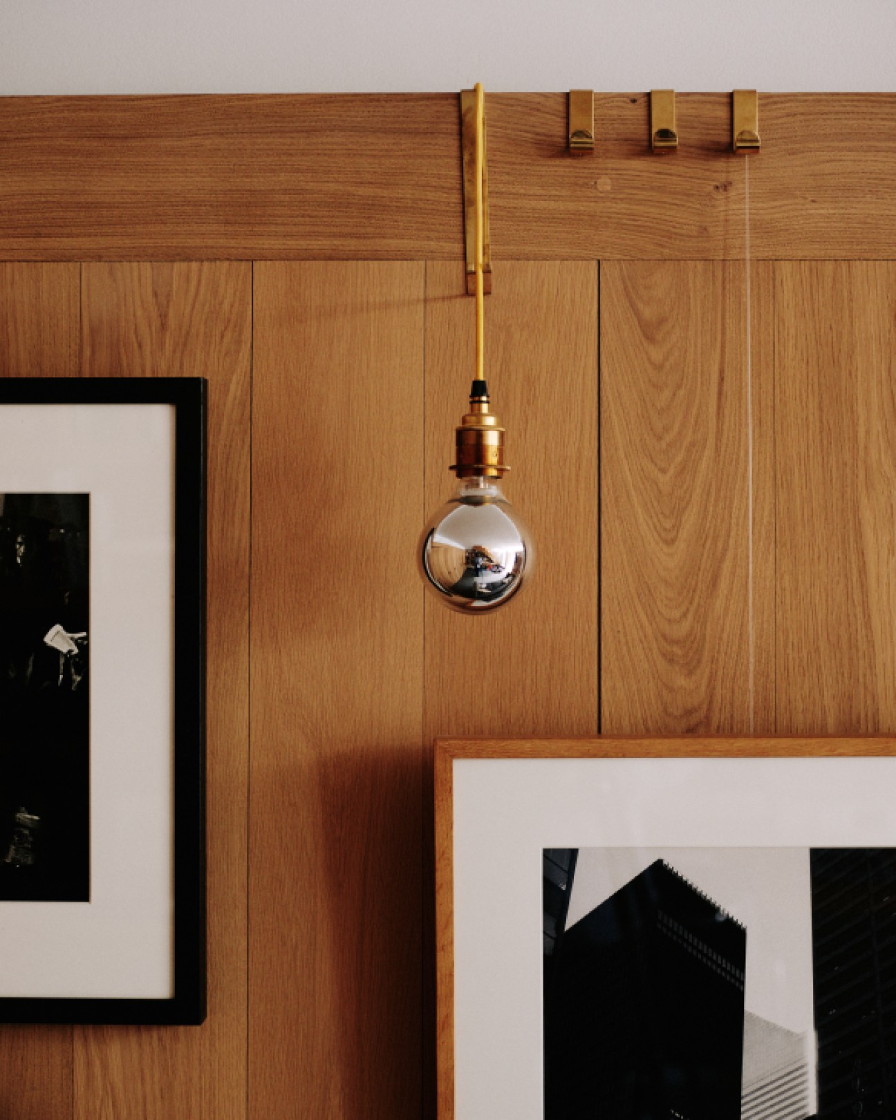Brass pendant lamp with spherical copper shade designed by architect William Smalley hanging against wooden wall paneling.