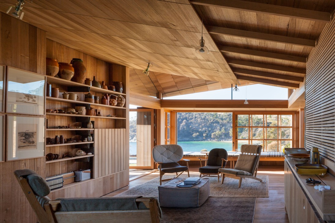 Modern living room with Tasmanian oak finishes, mid-century chairs, and large windows overlooking a coastal bay.