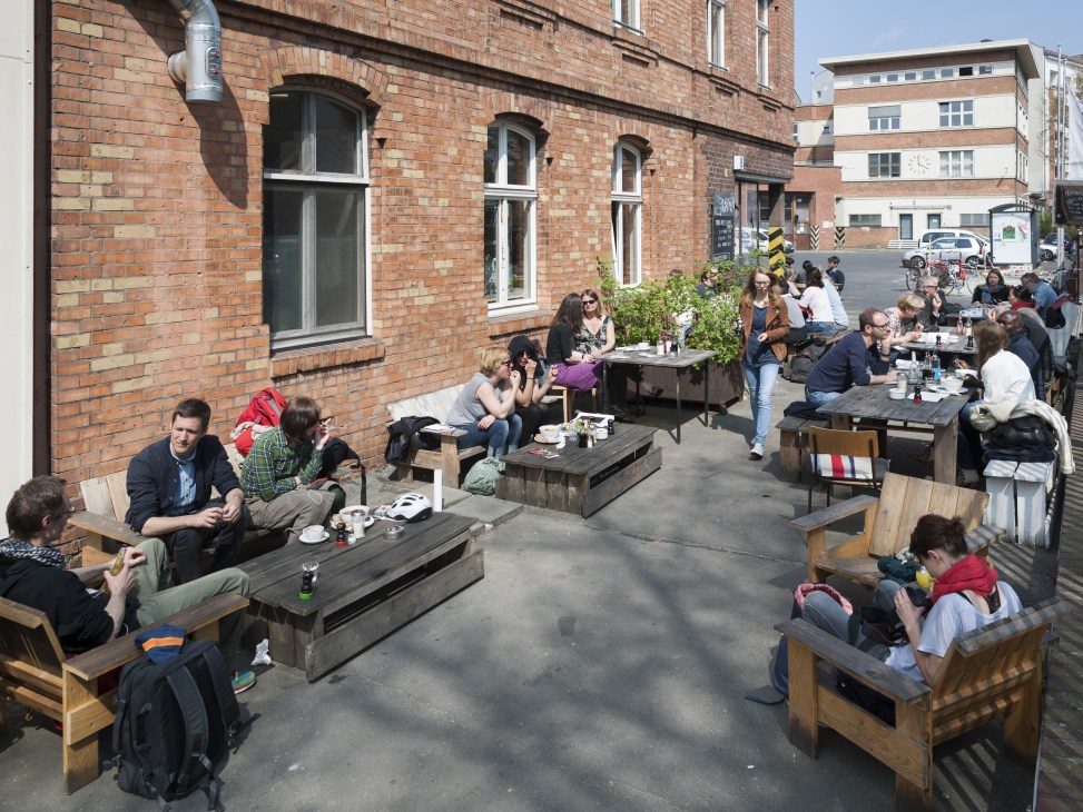 Outdoor seating area at Café Pförtner with numerous patrons enjoying beverages at wooden tables.