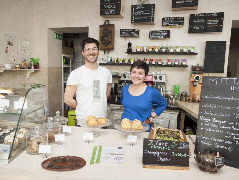 Paul and Tonia Meskunas stand behind the counter at TassenKuchen café with baked goods and menu boards.