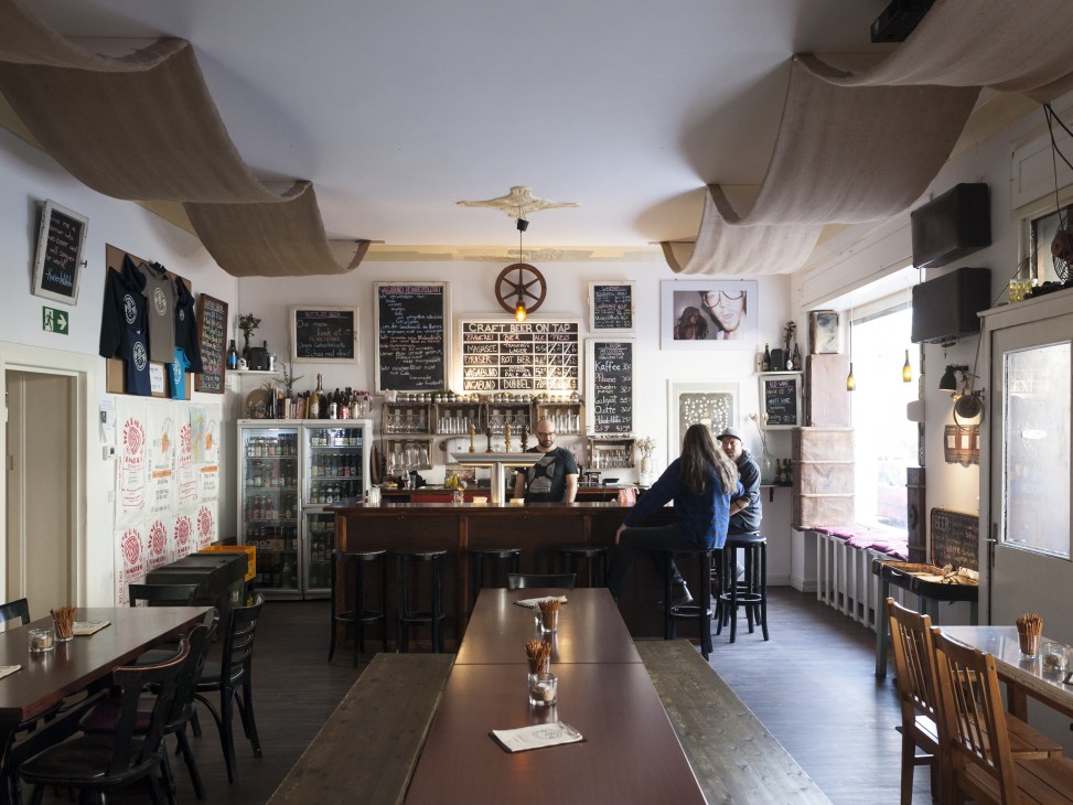 Interior of Vagabund Brauerei brewery with bar counter, draped ceiling, and patrons seated at tables.