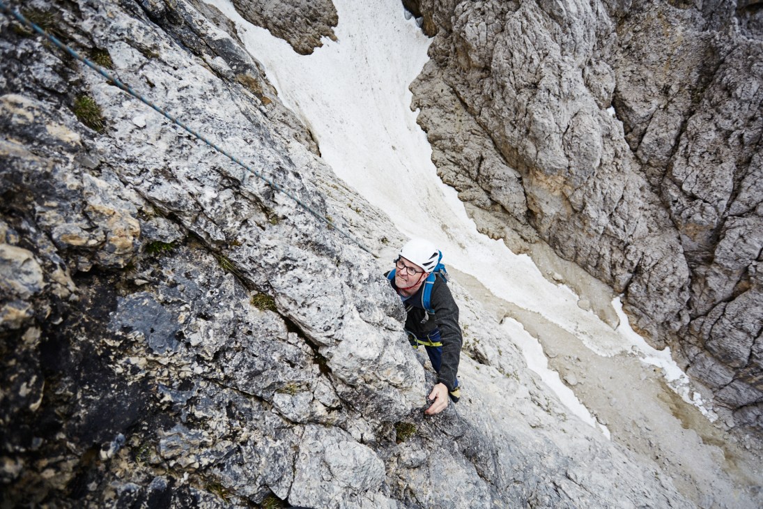 A climber scales a steep limestone rock face in Italy wearing protective gear and blue climbing rope.