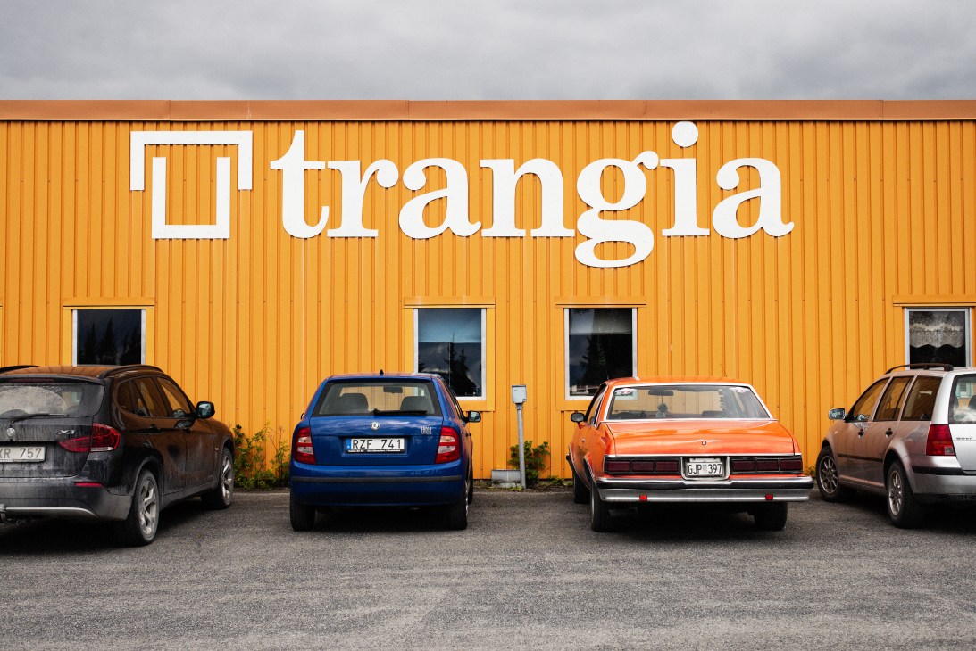 Trangia factory building with bright orange corrugated metal exterior and white lettering, parked cars in front.