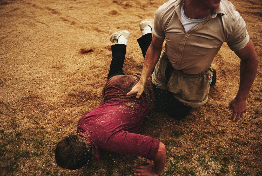 A Swiss wrestler in burgundy schwinghosen stands over his defeated opponent lying in the sawdust.