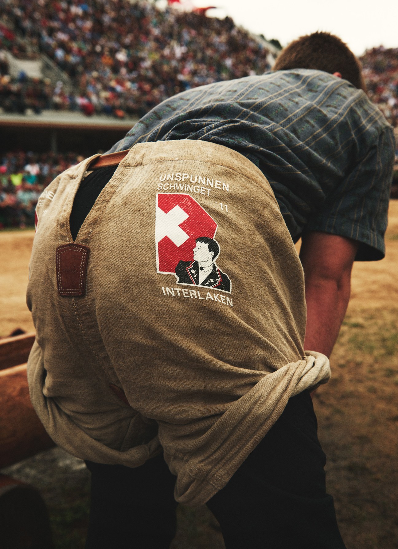 A Schwingen wrestler wears a traditional burlap jacket displaying the Swiss flag and Interlaken festival emblem at the Brünig event.