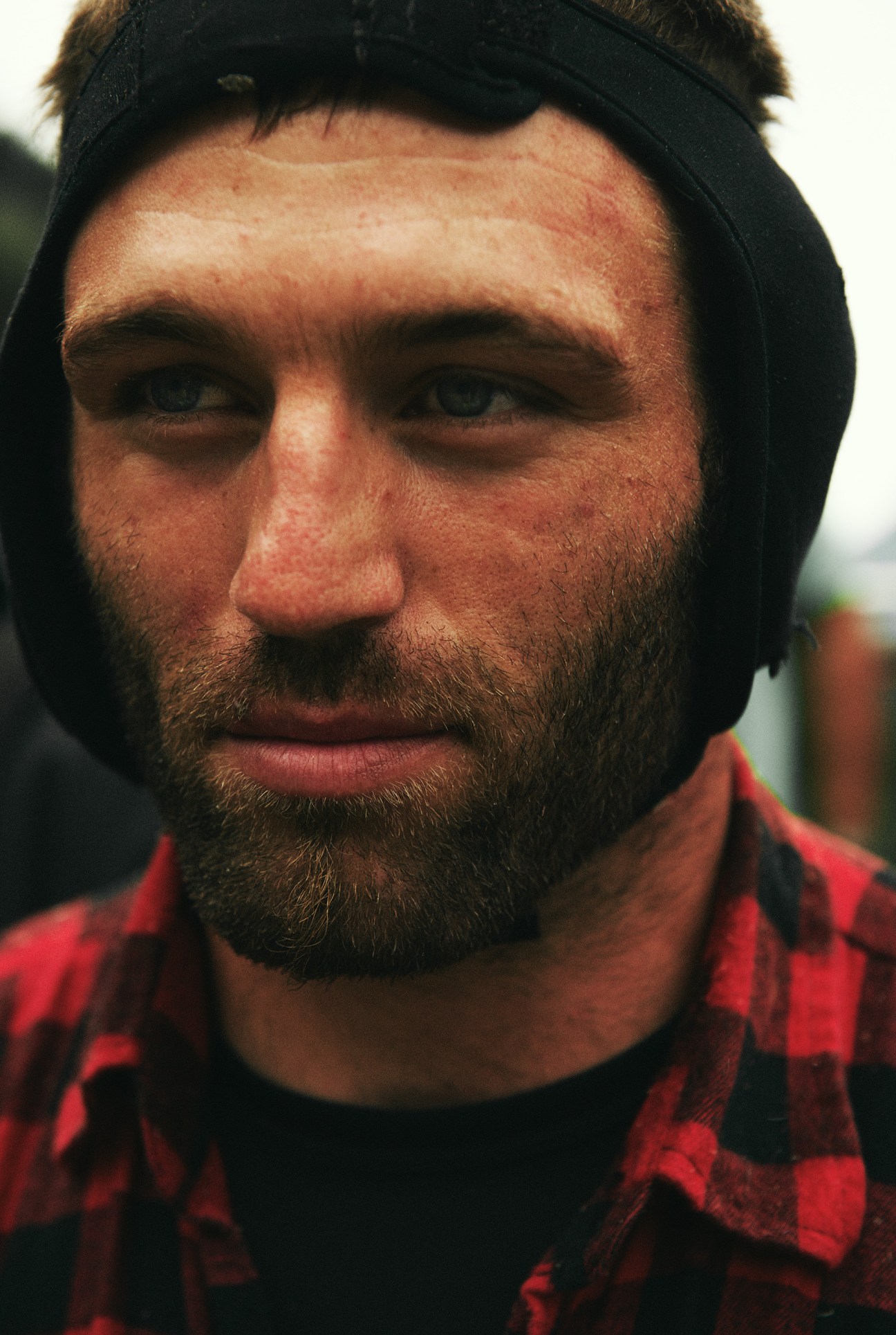 Close-up portrait of a bearded man wearing black ear-protecting headgear and a red plaid shirt.