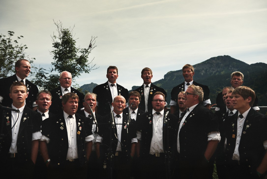 Brünig yodelling choir in traditional black jackets and white shirts performing outdoors with Alpine mountains in background.