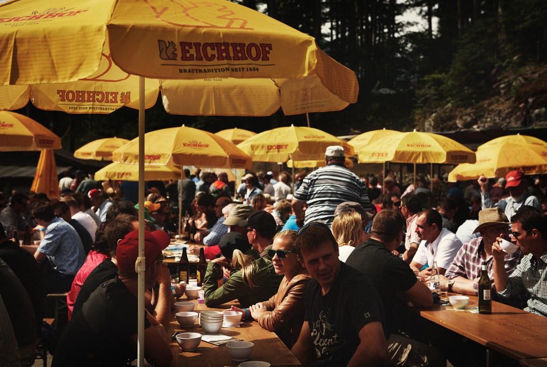 Spectators dining under yellow Eichhof umbrellas at outdoor picnic tables during the Brünig Schwingen wrestling event.