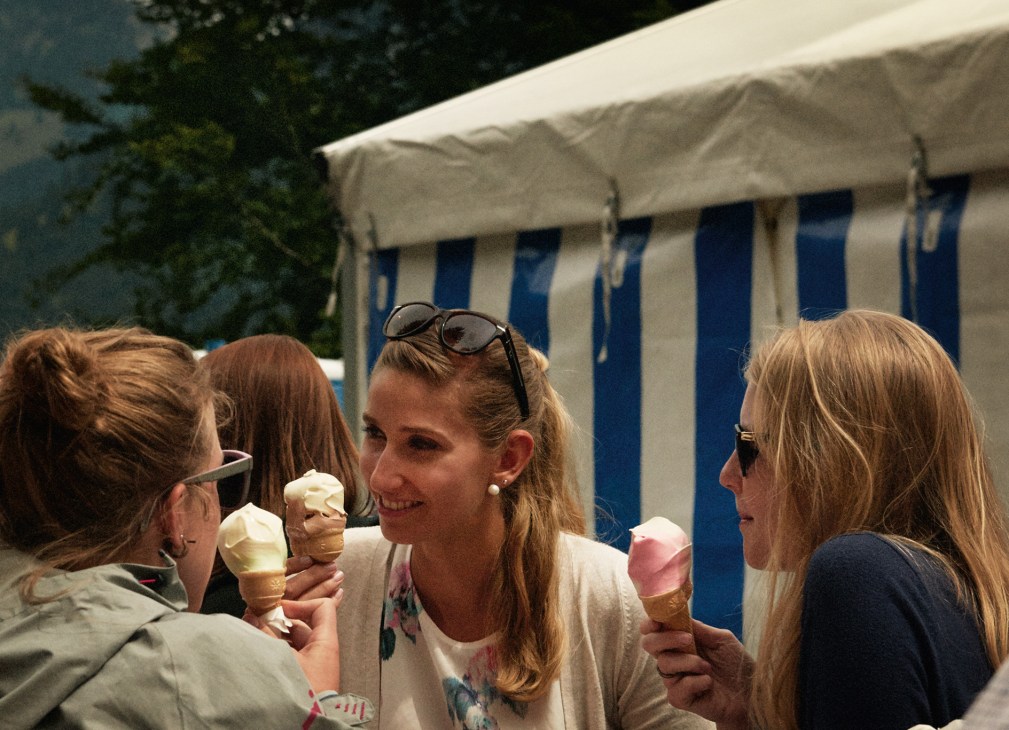 Women enjoying ice cream cones in front of blue and white striped beach huts.