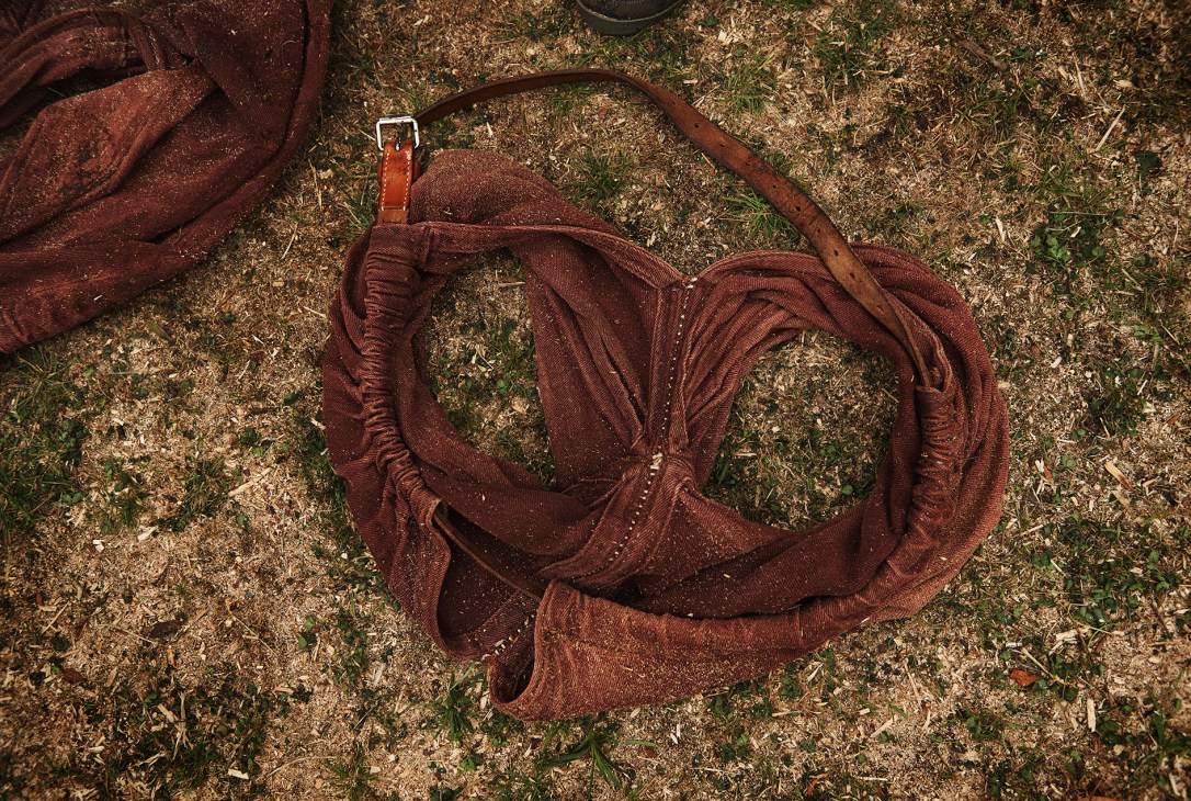 Red burlap Schwinghosen wrestling pants lying on sawdust and grass ground.