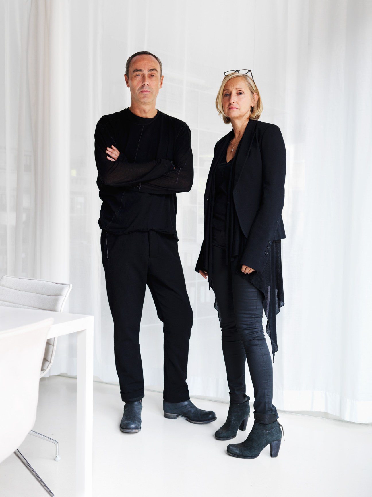 Two architects in black clothing stand in a minimalist white office space.