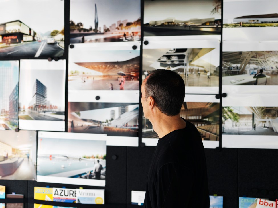 Architect Roman Delugan views a wall of printed architectural project photographs in the DMAA office.