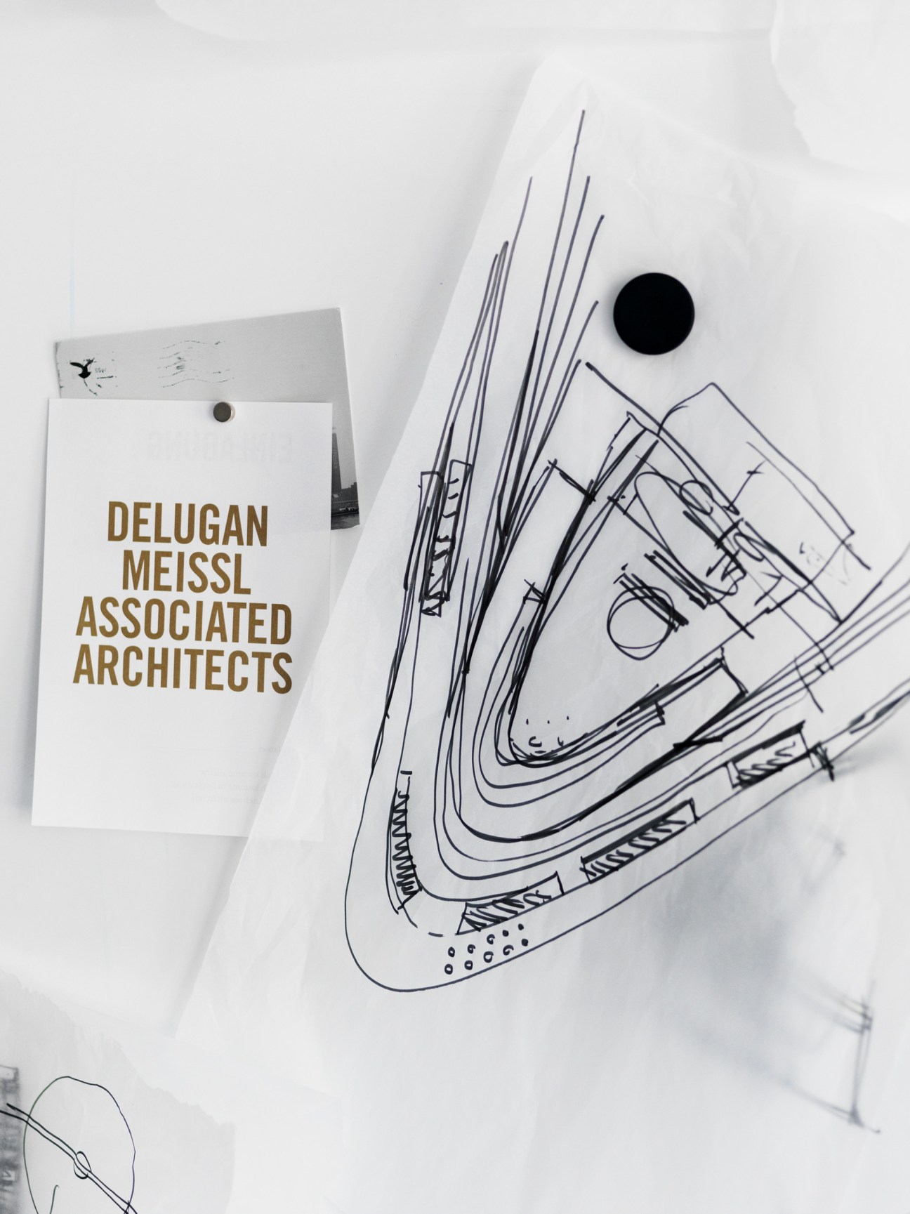 Architectural sketches and a folder labeled Delugan Meissl Associated Architects on white paper with a black circle.