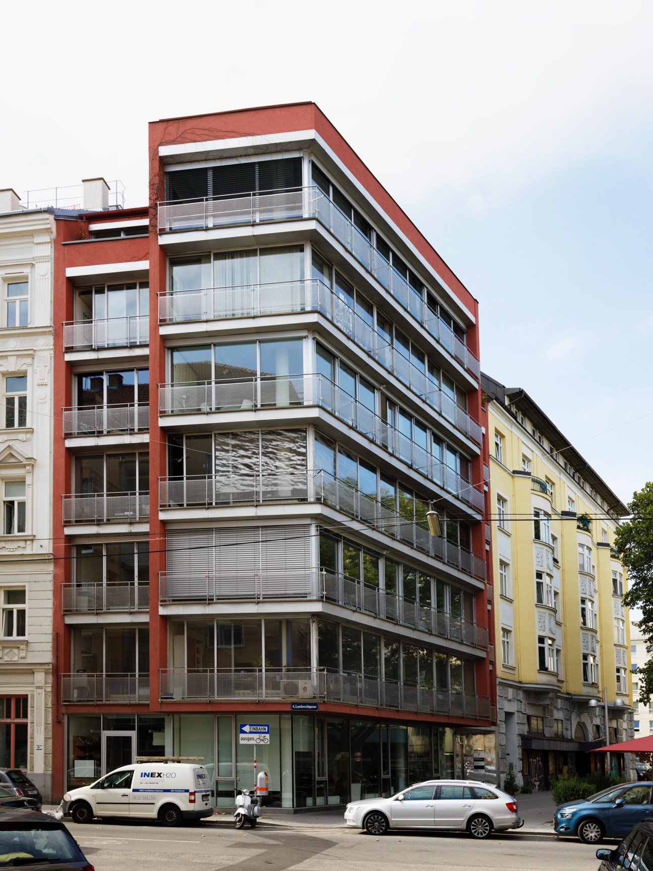 Modern red and grey residential building with balconies on a Vienna street corner.