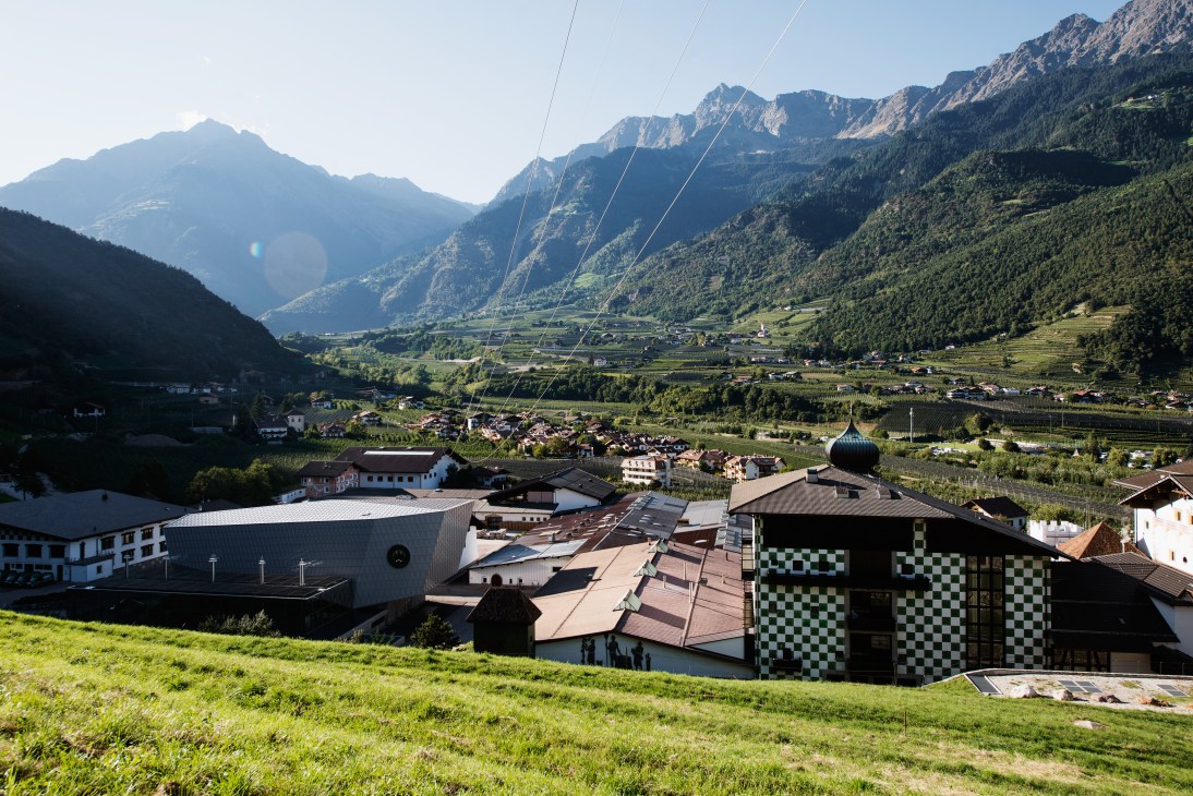 Forst brewery complex nestled in South Tyrolean Alpine valley with mountains and village in background.