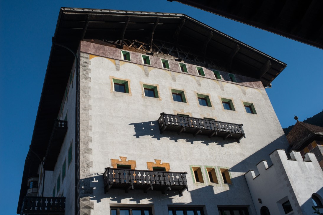 Historic white stone tower with green shutters and wooden balconies against a clear blue sky.