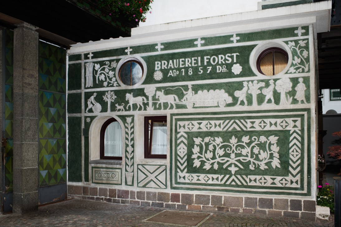 Decorative green and white mural facade of Brauerei Forst brewery entrance with ornamental patterns and historical scenes.