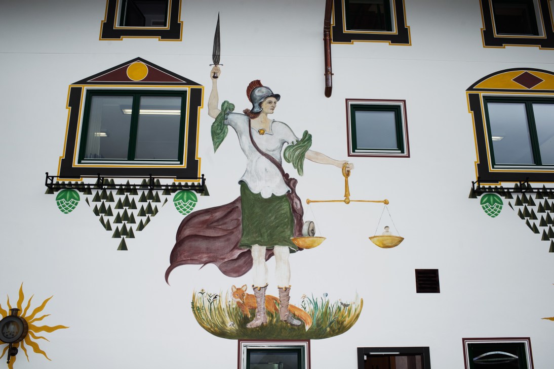Handpainted mural of allegorical figure holding scales with hop flowers and decorative windows on brewery wall.