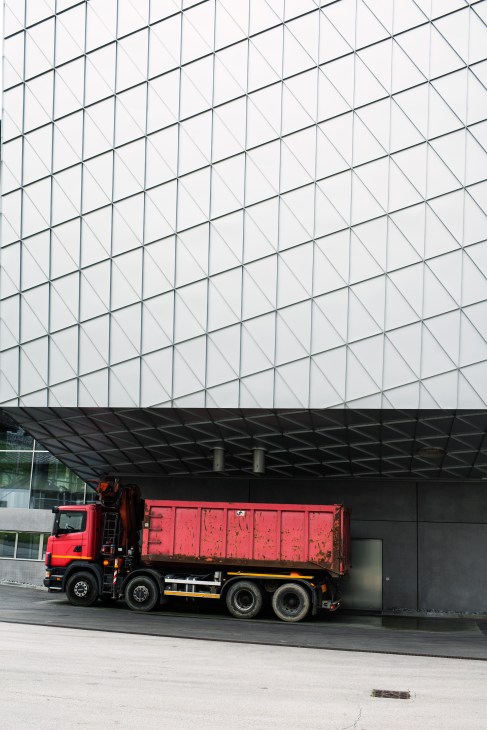 Red delivery truck parked beneath a geometric glass and steel brewery facade.