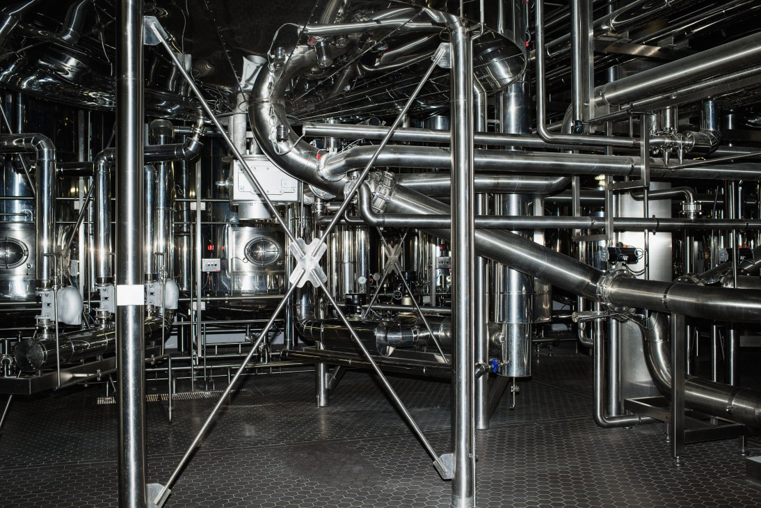Complex network of shiny stainless steel pipes and industrial brewing equipment in Forst brewery's production facility.