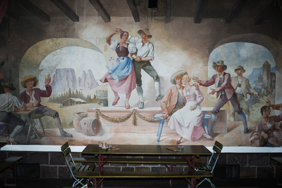 Tyrolean mural depicting Alpine villagers celebrating with beer and traditional music in a mountain setting.