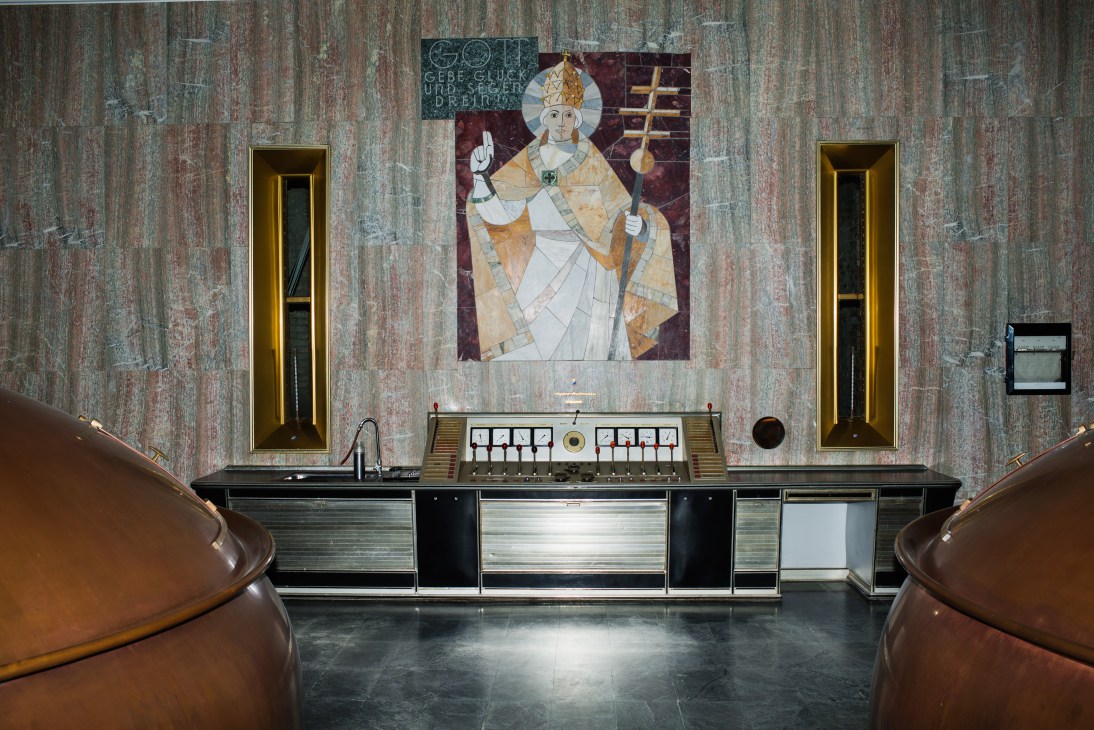 Control panel in brewery's old wing with weathered wooden wall, religious artwork, and brass-trimmed doors.