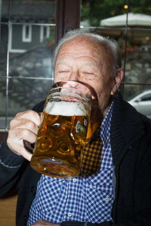 Elderly man drinking from a large glass mug of Forst beer outdoors.