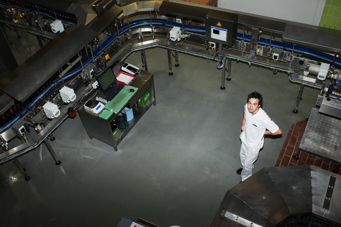 Technician in white uniform stands in Forst brewery's bottling plant with conveyor systems and equipment.