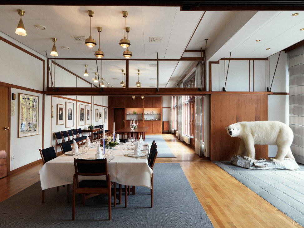 Formal dining room with white tablecloth, wooden chairs, pendant lights, and Edvard Munch graphic works on walls.