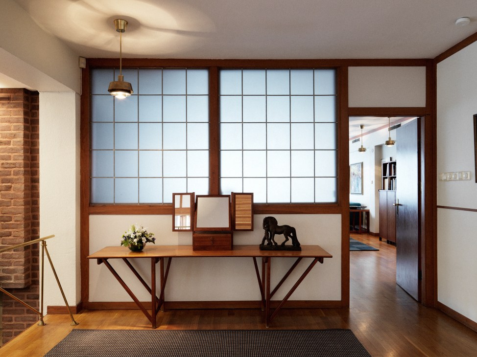 Entrance hall with teak-framed glass screens evoking Japanese shoji screens, wooden console table with flowers and sculpture.