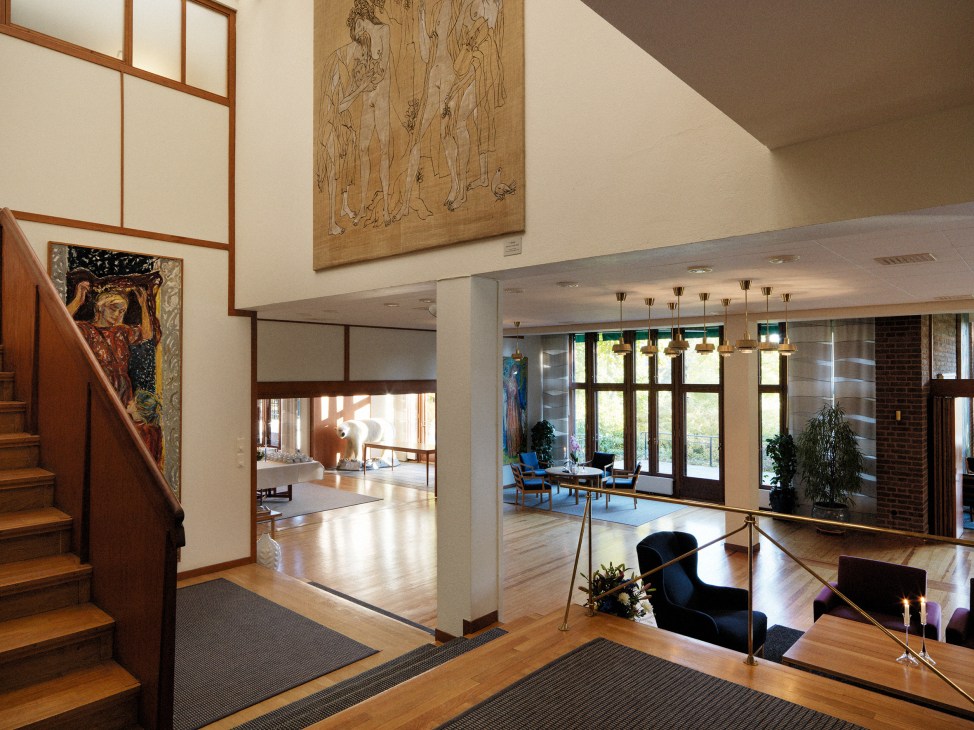 Spacious interior with wooden flooring, teak-framed elements, brass railings, and mid-century modern furnishings in the Norwegian embassy.