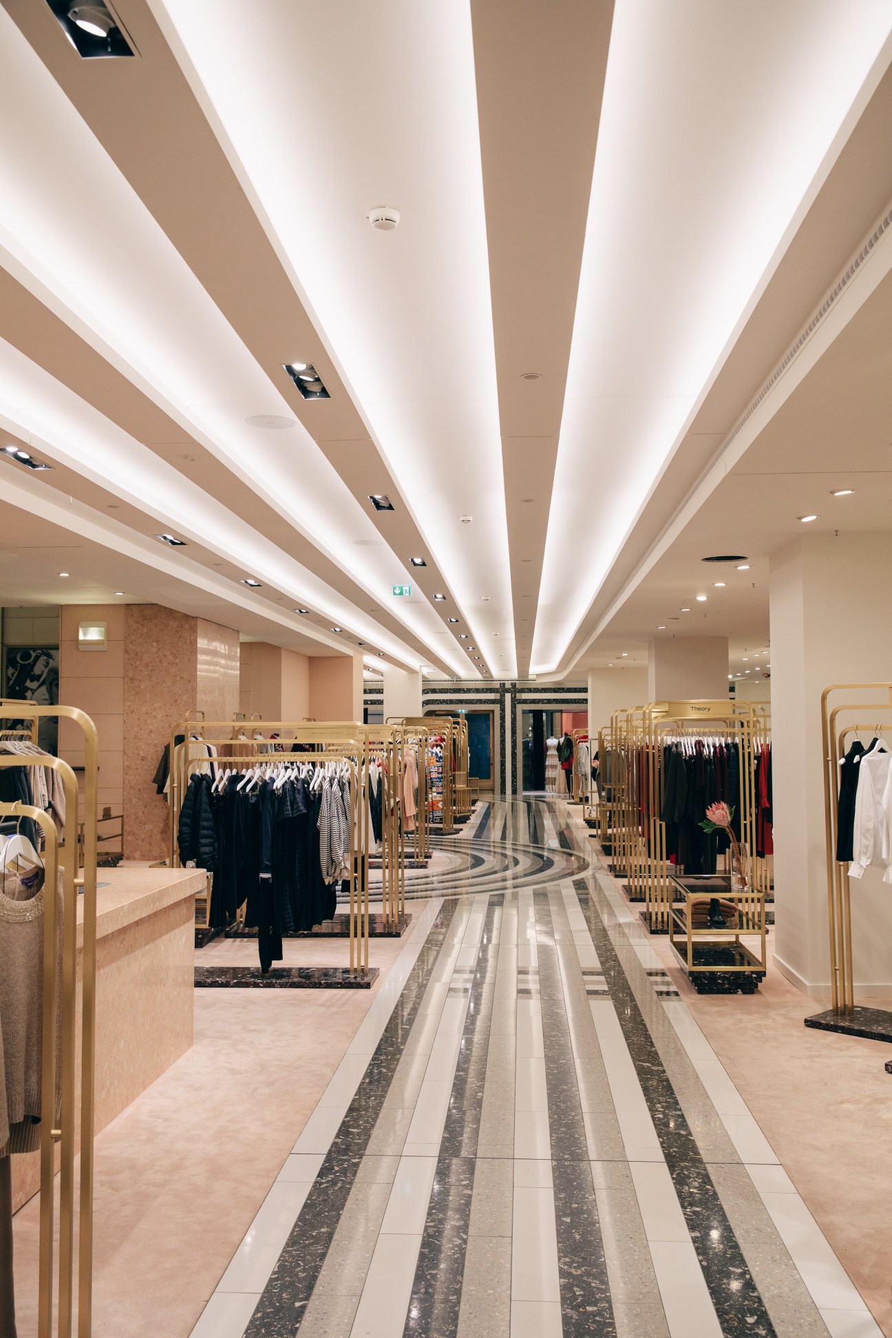 Interior of Kadewe's women's fashion department with marble floor stripes, gold clothing racks, and illuminated ceiling designed by India Mahdavi.