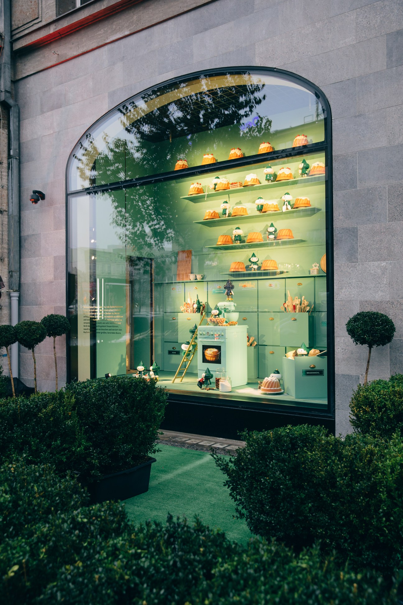 A striking green window display designed by Rem Koolhaas features orange pumpkins and figurines on illuminated shelves.