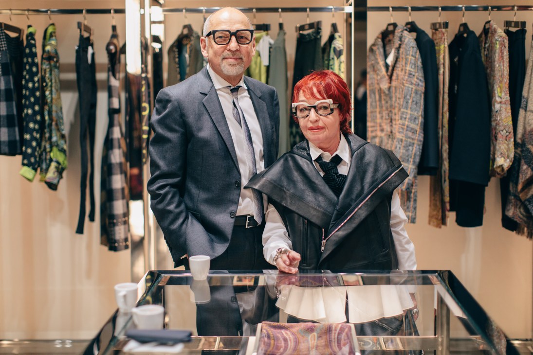 Burgi Schulze-Hewmann and her husband stand together in Kadewe's women's fashion department surrounded by hanging dresses.